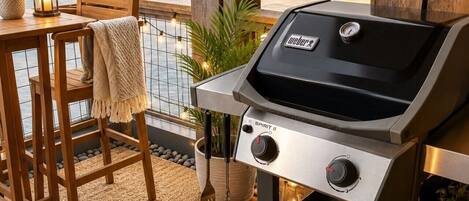An outdoor patio with a Weber Spirit II grill, wooden chairs, a table, and a view of the water.