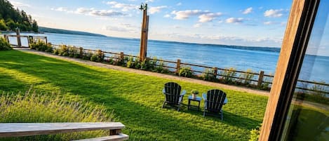Une terrasse enherbée avec deux chaises et une table, d’où l’on a vue sur une étendue d’eau et un phare.
