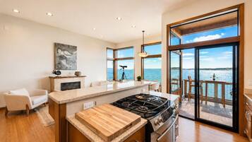 A modern kitchen with a large island, a gas stove, and a view of the sea through large windows.