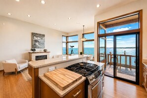 A modern kitchen with a large island, a gas stove, and a view of the sea through large windows.