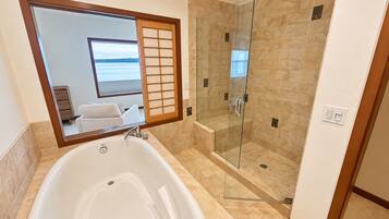 A bathroom with a bathtub, a glass-enclosed shower, and a large mirror reflecting a room with a view of the sea.