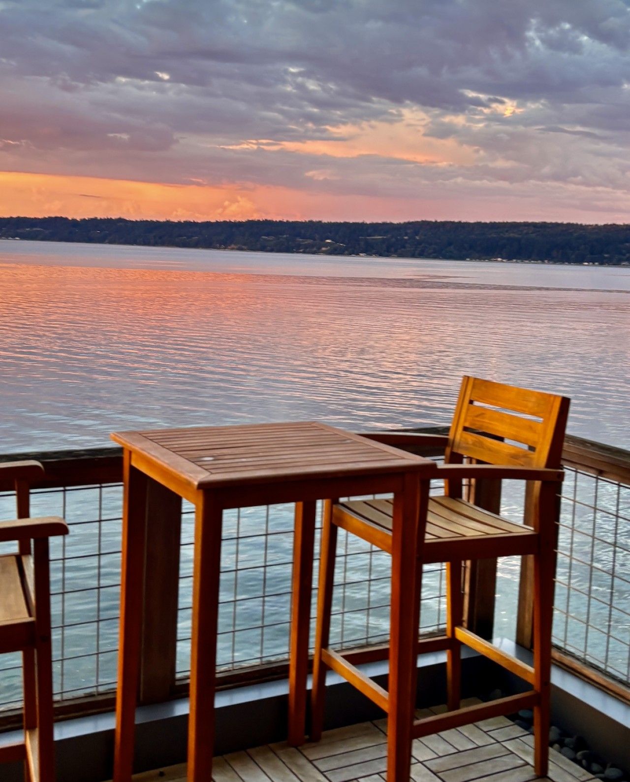 Een houten terras met een tafel en stoel, uitkijkend op het water tijdens zonsondergang.