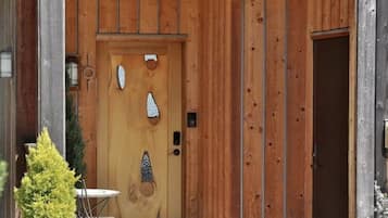 Une porte en bois ornée d’éléments décoratifs, une petite table et une plante en pot devant un bâtiment.