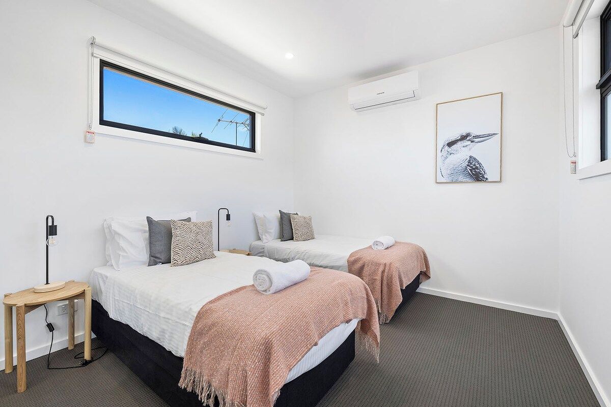 A hotel room with two beds, a window with a view, an air conditioning unit, and a framed picture on the wall.
