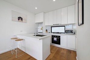 A modern kitchen with white cabinetry, a central island with stools, a built-in oven, and a microwave.