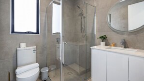 Et moderne badeværelse med en brusekabine i glas, toilet, vask med spejl og et vindue.