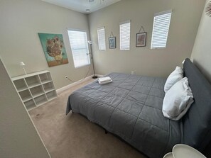 A bedroom with a bed, a painting, a lamp, and a window with blinds.