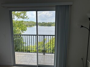 A room with a sliding glass door leading to a balcony with a view of a lake and trees.