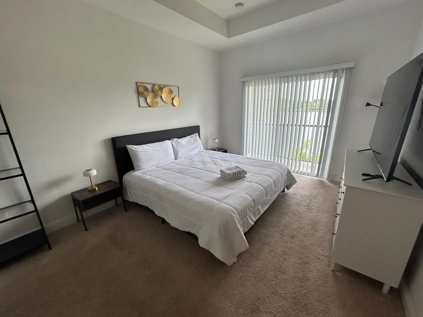 A bedroom with a bed, a nightstand, a TV, and a window with blinds.