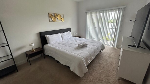 A bedroom with a bed, a nightstand, a TV, and a window with blinds. - Condo House 20 min from the Disneyland (Davenport)