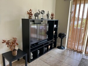 Una sala de estar con un mueble negro para entretenimiento, una mesita con un florero y un ventanal con cortinas.