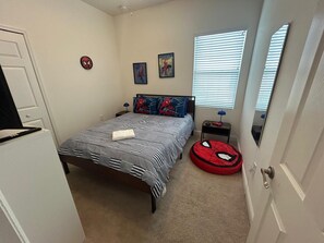 Un dormitorio con cama, un sillón de peluche con temática de Spider-Man, una mesita de noche y una ventana con persianas.