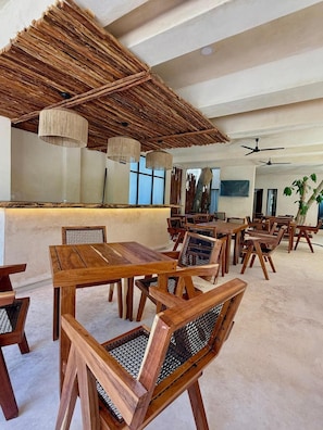 A restaurant interior with wooden furniture, a thatched ceiling, and hanging pendant lights. - Joanza By Ool Hotels (Isla Holbox)