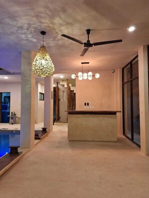 A modern interior with a ceiling fan, pendant lighting, a bar area, and a pool. - Joanza by OOL Hotels (Isla Holbox)