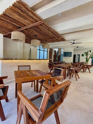 A spacious indoor dining area with wooden tables and chairs, a thatched ceiling, and pendant lighting. - Joanza by OOL Hotels (Isla Holbox)