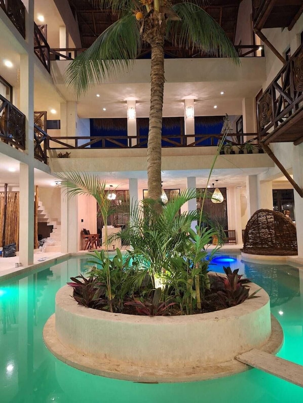A multi-level indoor pool area with a central palm tree, surrounded by various plants and a circular seating area. - Joanza By Ool Hotels (Isla Holbox)