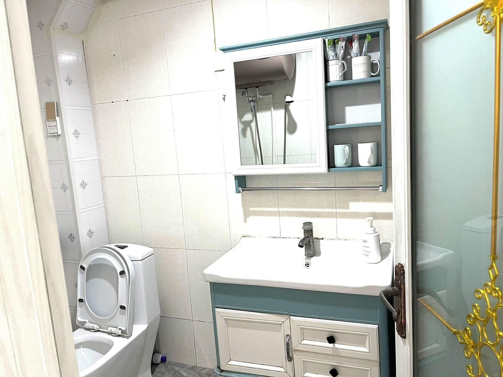 A bathroom with a toilet, sink, mirror, and storage cabinets.