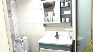 A bathroom with a toilet, sink, mirror, and storage cabinets.