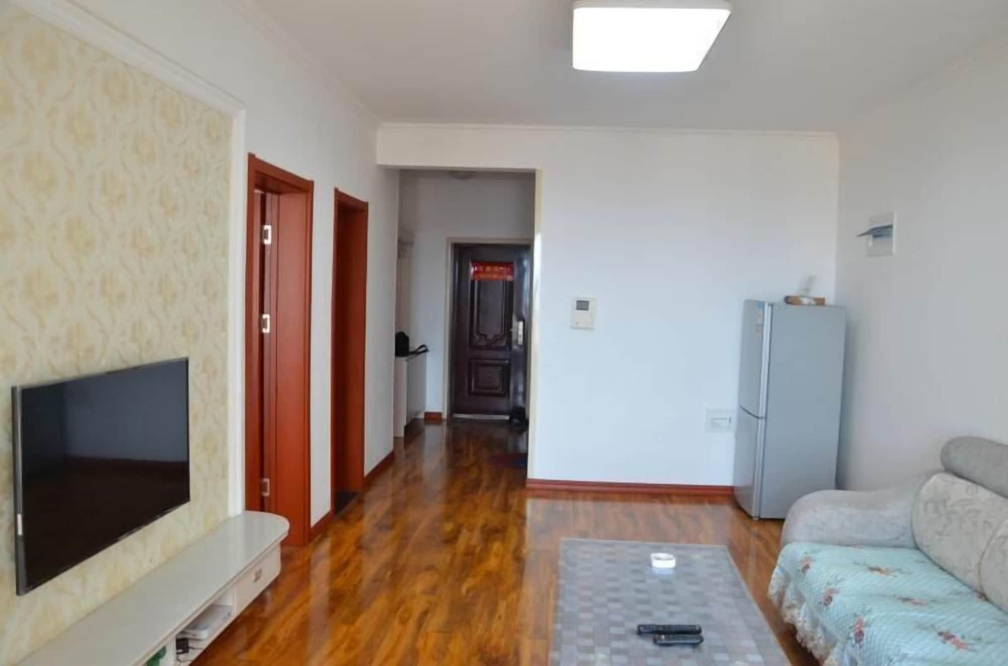 A living room with a flat-screen TV, a sofa, a patterned carpet, and a refrigerator.