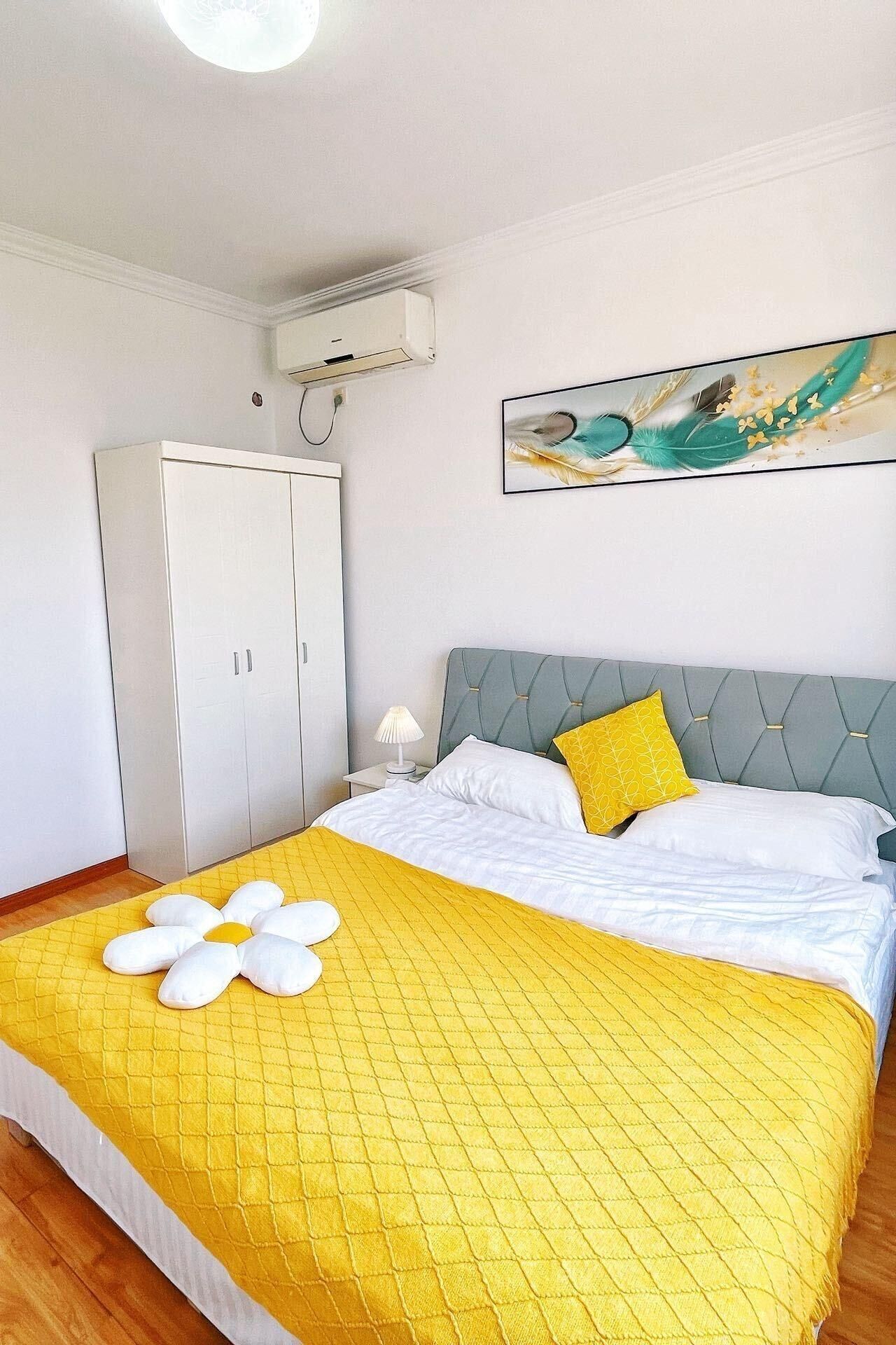 A hotel room with a bed, a wardrobe, a painting, and an air conditioning unit.