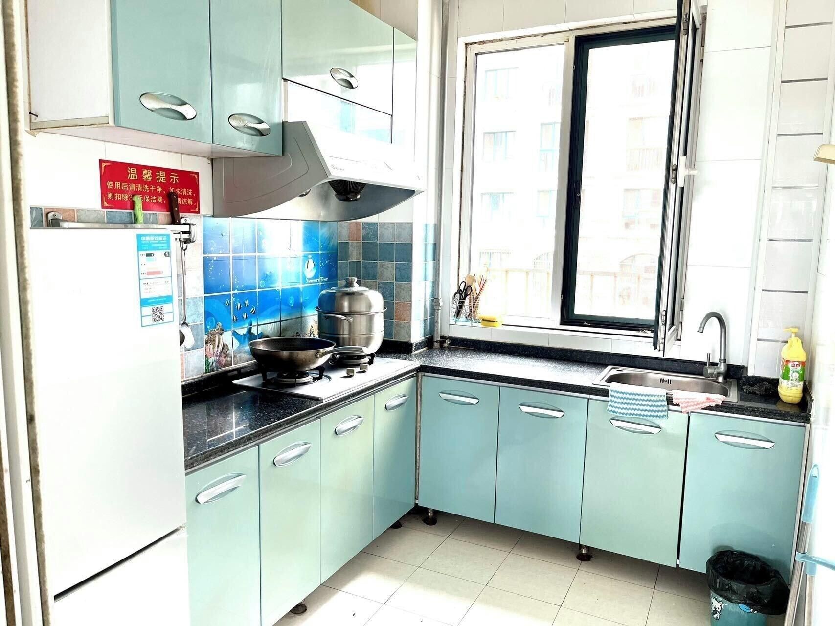 A kitchen with light blue cabinets, a stainless steel range hood, a window, and a sink.