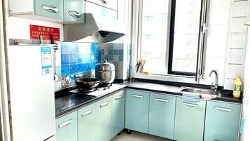 A kitchen with light blue cabinets, a stainless steel range hood, a window, and a sink.