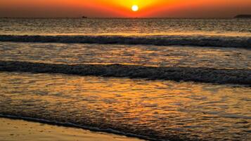 A sunset over a calm sea with waves gently lapping onto the shore.
