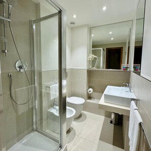 A modern bathroom with a glass-enclosed shower, a toilet, and a sink with a mirror above. - Bay Village (Cervia)