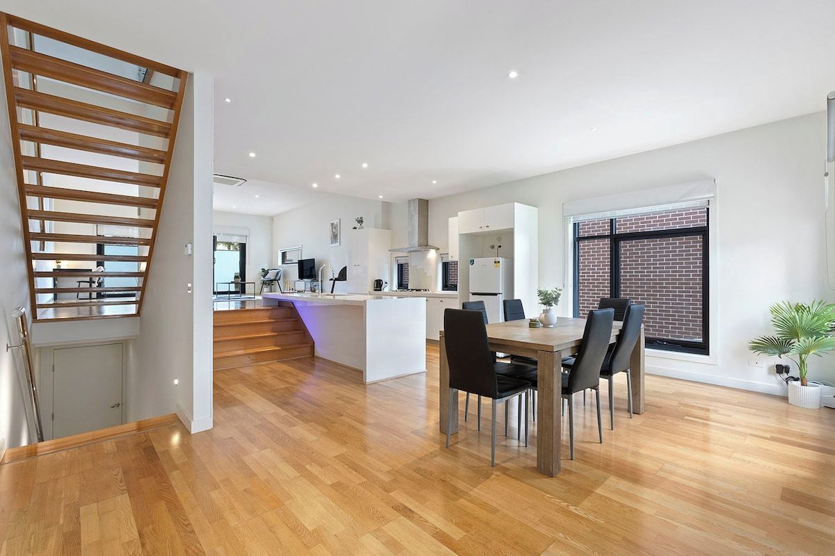 A modern kitchen with white cabinetry, a central island, and a dining area with a wooden table and chairs.