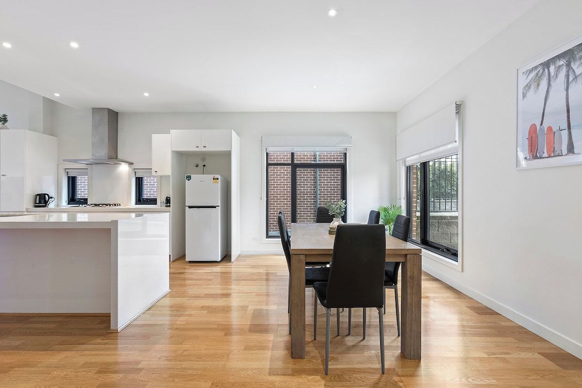 A modern kitchen with white cabinetry, a central island, and a dining area with a wooden table and chairs.