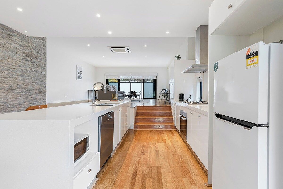 A modern kitchen with white cabinetry, a built-in oven, and a stainless steel refrigerator.