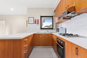 Cocina moderna con armarios de madera, estufa a gas, microondas y ventana con vistas al exterior.
