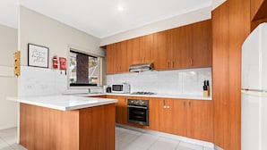 A modern kitchen with wooden cabinets, a white countertop, a built-in oven, and a microwave. - Domi Rentals - The Stockdale Home (Clayton)