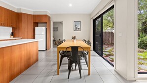 A modern kitchen with wooden cabinets, a white countertop, and a dining area with a wooden table and chairs. - Domi Rentals - The Stockdale Home (Clayton)