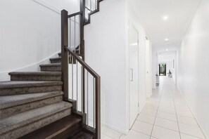 A staircase with a dark wooden handrail and carpeted steps leading to a white door. - Domi Rentals - The Third Residence (Clayton South)