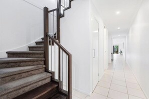 A staircase with a wooden handrail and carpeted steps leading to a white door. - Domi Rentals - The Third Residence (Clayton South)