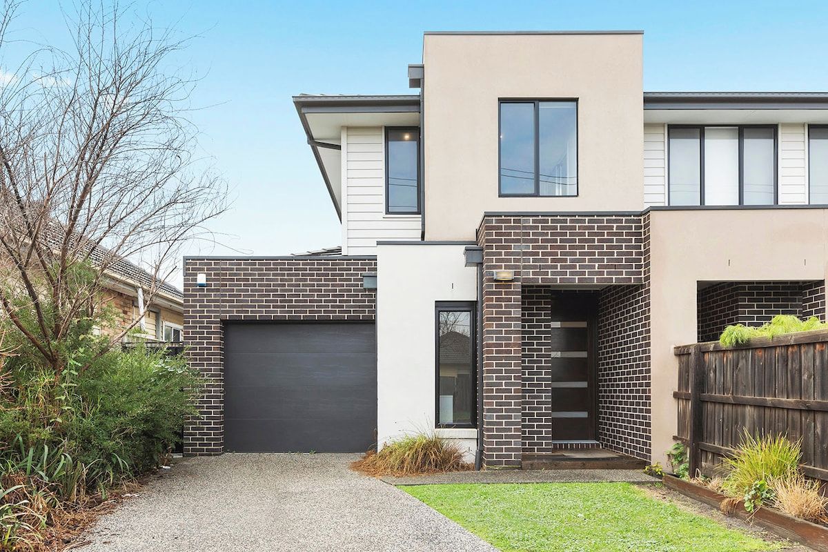 A modern two-story house with a garage, a brick facade, and a small front yard.