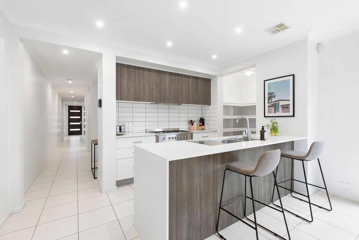 A modern kitchen with a central island, bar stools, and a view into the adjacent living area.