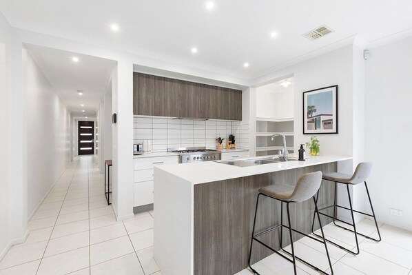 A modern kitchen with a central island, bar stools, and a view into the adjacent living area.