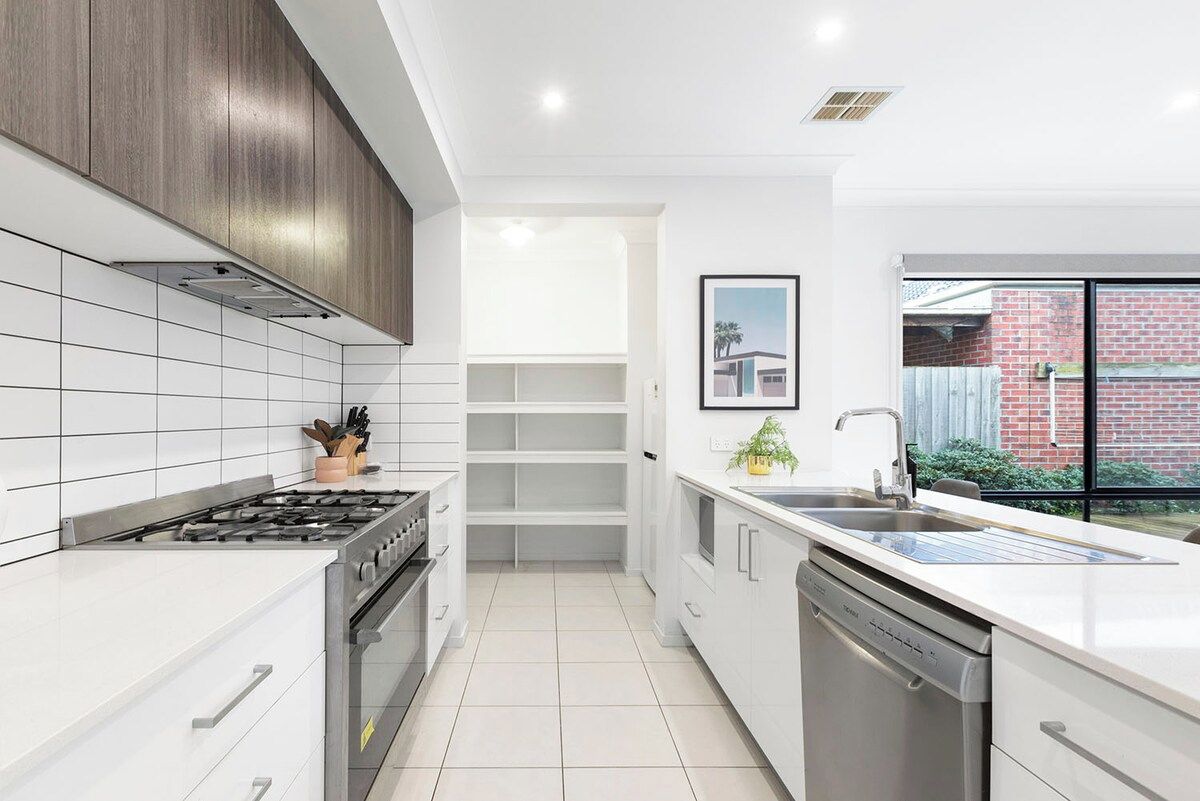 A modern kitchen with white cabinetry, a gas stove, a dishwasher, and a window with a view of a brick building.