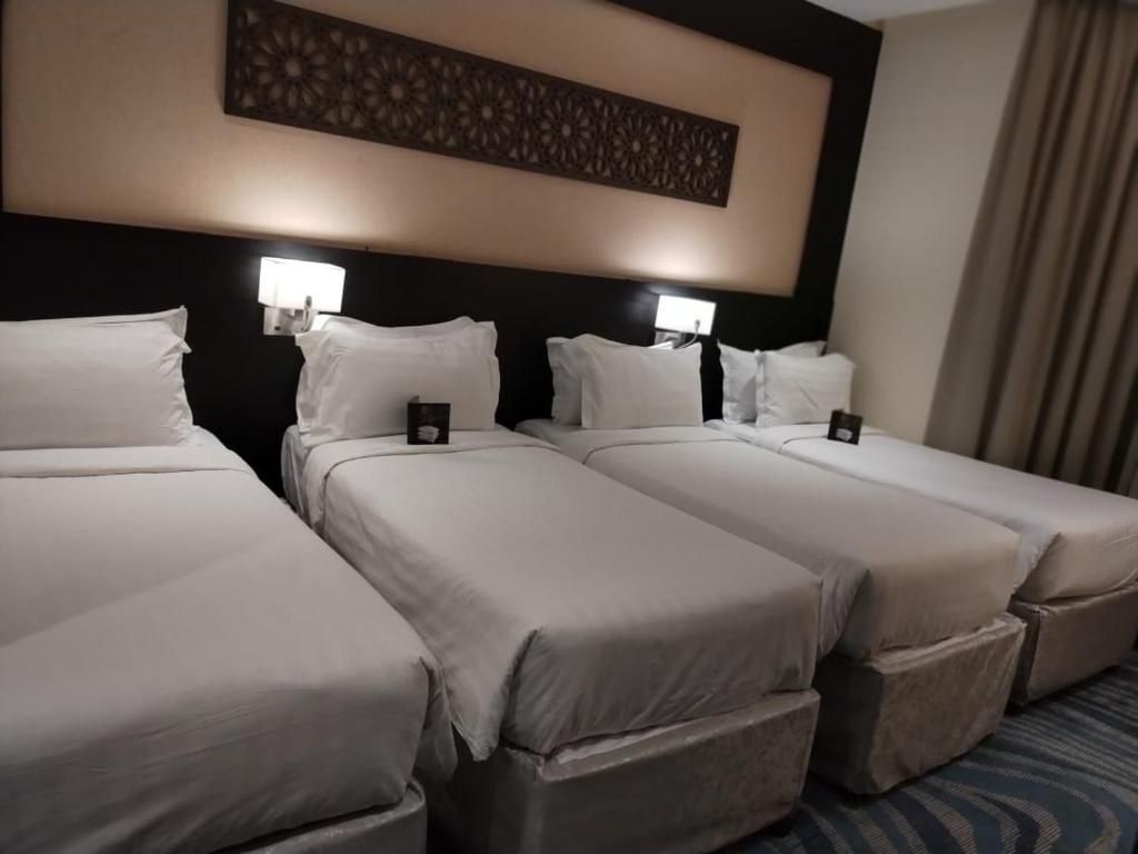 A hotel room with three single beds, each with a pillow and a small bedside table.