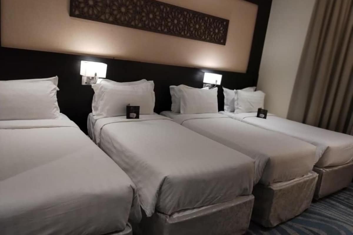 A hotel room with three single beds, each with a pillow and a small bedside table.