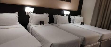 A hotel room with three single beds, each with a pillow and a small bedside table.