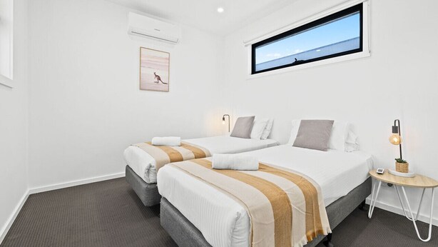 Et hotelværelse med to senge, et vindue med udsigt, en aircondition, et lille bord med en lampe og et billede i ramme på væggen.