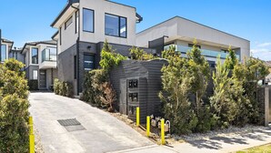 Et moderne hus med to etager og en indkørsel, omgivet af grøn bevoksning under en klar himmel.