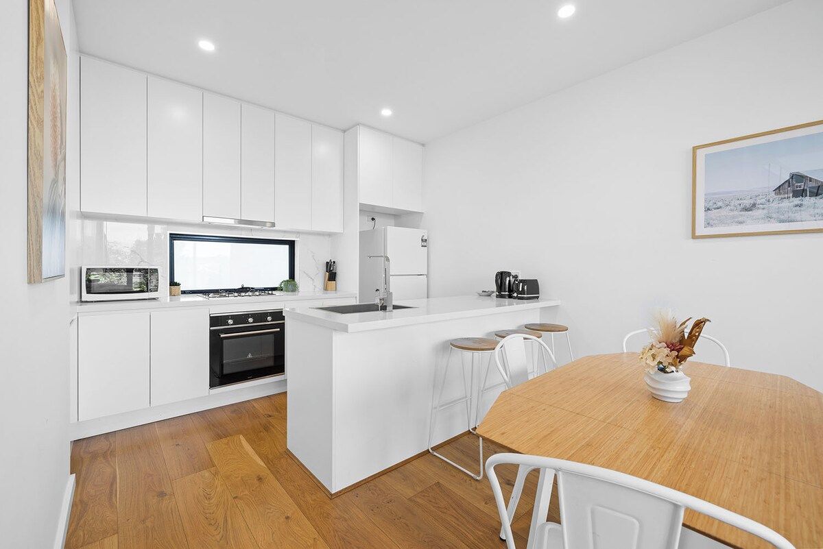 A modern kitchen with white cabinetry, a central island, and a dining area with a wooden table and white chairs.