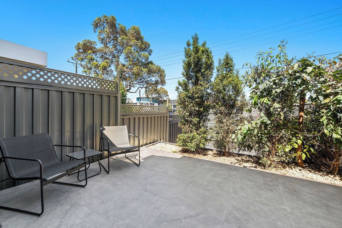An outdoor patio area with a metal fence, two chairs, and a small garden.