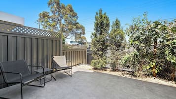 An outdoor patio area with a metal fence, two chairs, and a small garden.