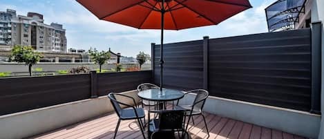 Una terraza en la azotea con una mesa y sillas, un paraguas rojo y vistas a edificios en el fondo.