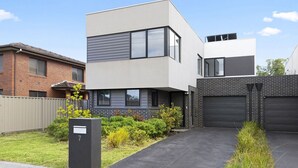 Une maison moderne à deux étages, dotée d’un garage, d’une boîte aux lettres et d’une pelouse bien entretenue.